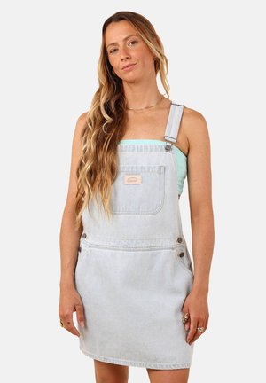 Robe salopette en denim bleu clair avec bretelles ajustables, poche avant et boutons sur le côté. Texture lisse, design mi-genoux, branding minimaliste.