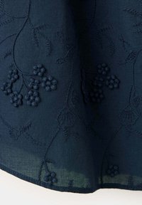 Tissu bleu foncé avec broderie florale en relief comprenant de petites fleurs regroupées et des motifs délicats de vigne.
