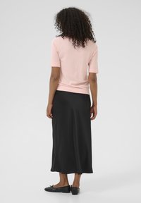 Un pull rose clair à manches courtes associé à une jupe maxi en satin noir, présentant une texture lisse et un design simple et élégant.