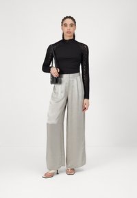 Black lace long-sleeve top paired with shiny silver wide-leg pants. Model holds a small black handbag and wears open-toed heels.