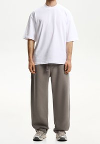 Weißes, übergroßes Baumwoll-T-Shirt mit kurzen Ärmeln, kombiniert mit grauen, locker sitzenden Sweatpants mit Seitentaschen und Kordelzug. Sportliche Schuhe.