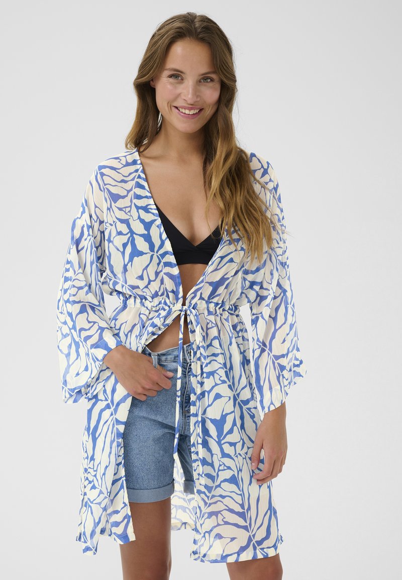 Kimono ligero, de estampado azul y blanco, con mangas largas y un lazo en la cintura, usado sobre un bikini negro y pantalones cortos de mezclilla.