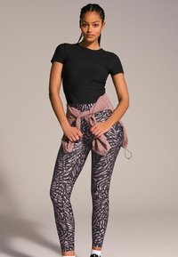 Svart kortärmad topp med mönstrade leggings i mörklila och rosa toner, lager på lager med en mauve jacka knuten i midjan.