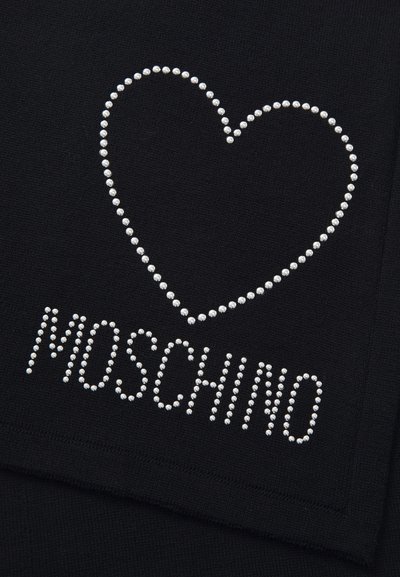 Estudantes prateados formam uma forma de coração acima da palavra "MOSCHINO" em tecido preto, provavelmente parte de uma peça de roupa ou acessório.