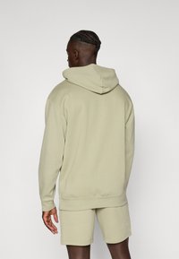 Hoodie vert clair avec une finition texturée, doté d'une grande capuche, de manches côtelées et d'un short assorti. Design simple et décontracté.