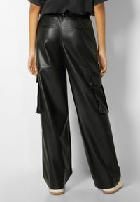 Svarta byxor i fusk läder med vida ben och cargofickor, hög midja samt en slät, glänsande yta.