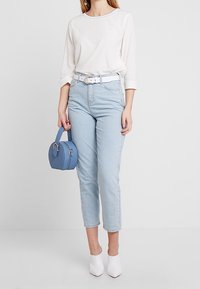 Jeans azzurri chiari con vita alta e gamba dritta, abbinati a una camicia bianca a maniche lunghe e una piccola borsa rotonda blu. Scarpe bianche con tacco.