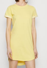 Robe t-shirt en coton jaune avec des manches courtes, un col rond et des finitions ourlées. Le tissu a une texture lisse et une coupe décontractée.