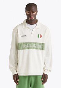 Maglietta da rugby a maniche lunghe in crema con una striscia verde. Presenta la scritta ricamata "PALMES" e una toppa con la bandiera italiana. Tessuto morbido e vestibilità rilassata.