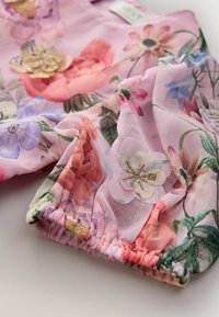 Leichter Stoffoberteil mit floralen Motiven in Pink, ausgestattet mit zarten bestickten Blumen und elastischen Bündchen. Glatte Textur mit bunten Blumenmustern.