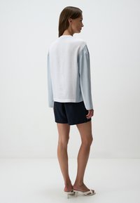 Top azzurro chiaro a maniche lunghe con retro in lino bianco, abbinato a pantaloni corti blu navy. Accenti bianchi ai polsini e all'orlo. Tessuto liscio e texture.