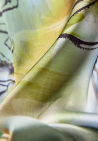 Seidenstoff mit einem sanften Glanz, der eine Mischung aus grünen, blauen und gelben Farbtönen aufweist und ein dezentes abstraktes Muster sowie eine glatte Textur zeigt.