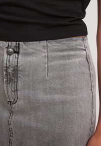 Falda de denim gris con un diseño ajustado, que cuenta con un botón frontal visible, bolsillos estándar y un acabado texturizado.