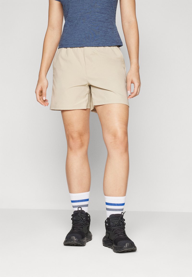 Beige, lätta shorts med elastiskt midjeband, tillsammans med svarta vandringskängor och vita strumpor med blå ränder.