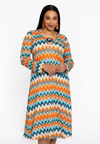 Langärmliges Kleid mit Zickzackmuster in Orange, Türkis und Weiß. Verfügt über einen runden Ausschnitt mit einem Schlüssellochdetail und einer fließenden Silhouette.