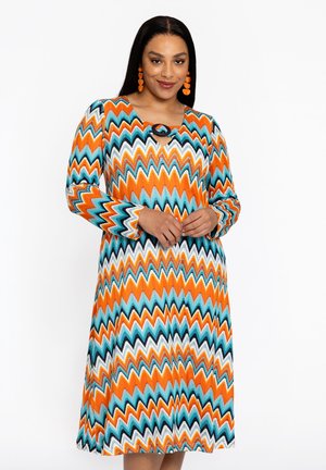 Robe à manches longues avec un motif en zigzag orange, turquoise et blanc. Présente un col rond avec un détail en trou de serrure et une silhouette fluide.