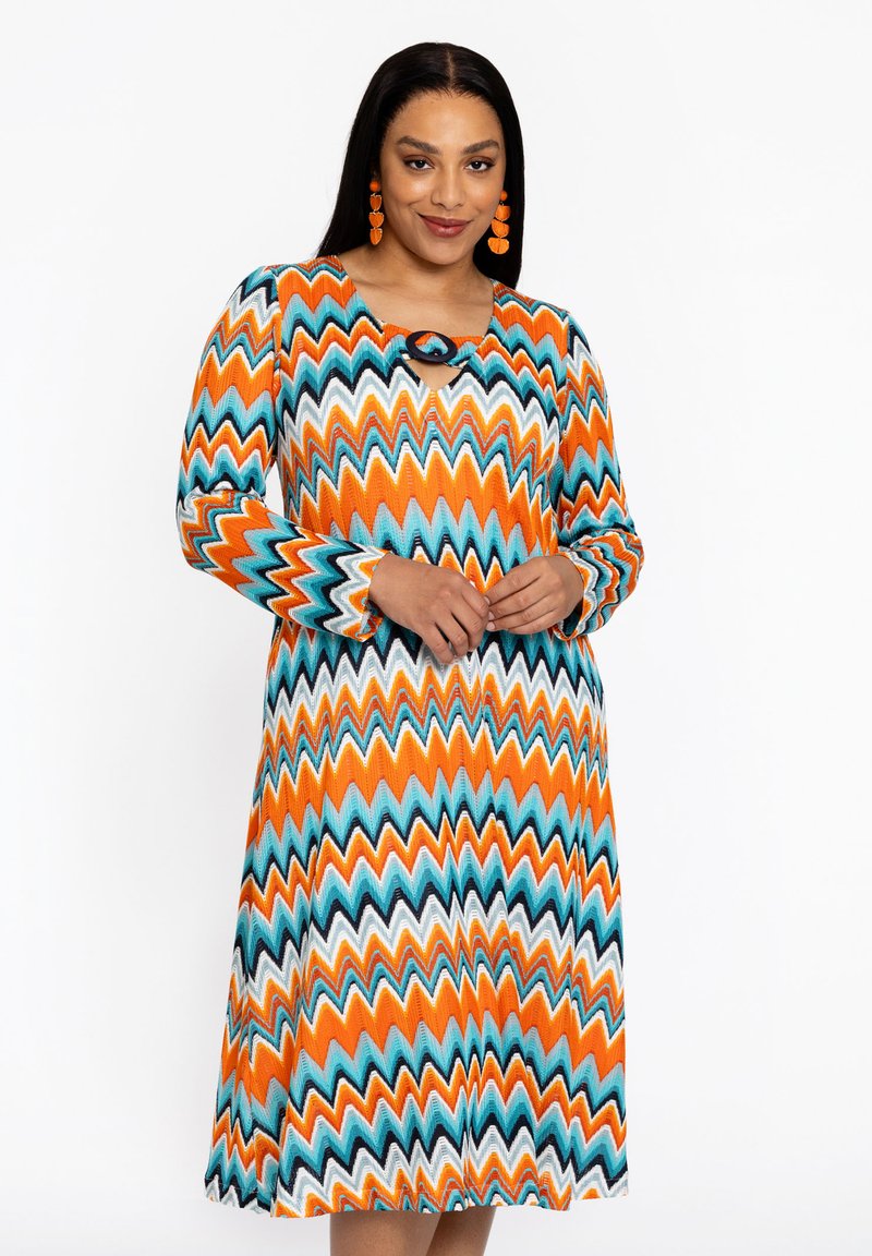 Langärmliges Kleid mit Zickzackmuster in Orange, Türkis und Weiß. Verfügt über einen runden Ausschnitt mit einem Schlüssellochdetail und einer fließenden Silhouette.