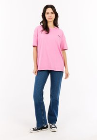 Roze oversized t-shirt met korte mouwen en een ronde halslijn, gecombineerd met blauwe recht gesneden jeans en zwarte canvas sneakers.