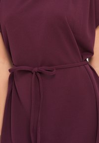 Μπλούζα μπορντώ με άνετη γραμμή, διαθέτοντας ζώνη δεμένη στη μέση και απαλό, ρέον υφασμάτινοTexture.