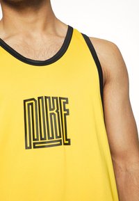 Débardeur sans manches jaune en tissu lisse, avec un logo "NIKE" en contour noir sur le devant et un col noir contrastant.