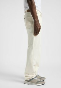 Jeans clairs à coupe straight, avec des poches arrière et des détails de couture subtils. Associés à des baskets grises.