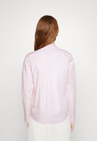 Camicia a maniche lunghe rosa chiaro realizzata in tessuto con righe verticali bianche, dotata di colletto a bottone e polsini a bottone singolo.