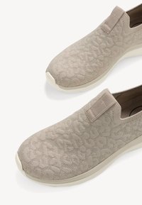 Bežové slip-on topánky vyrobené z textúrovanej pleteniny s jemným vzorom. Podrážka je biela s mierne vyvýšeným dizajnom, čo poskytuje kontrast.