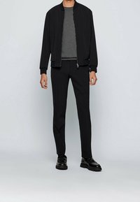 Czarna kurtka bomberka na szarym swetrze z okrągłym dekoltem, w połączeniu z czarnymi zwężanymi spodniami i masywnymi czarnymi butami. Gładka tkanina i minimalistyczny design.