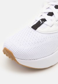 Baskets blanches avec une tige texturée, des accents noirs et une semelle beige. Elles sont dotées d'une semelle rembourrée et d'un design en maille respirante.