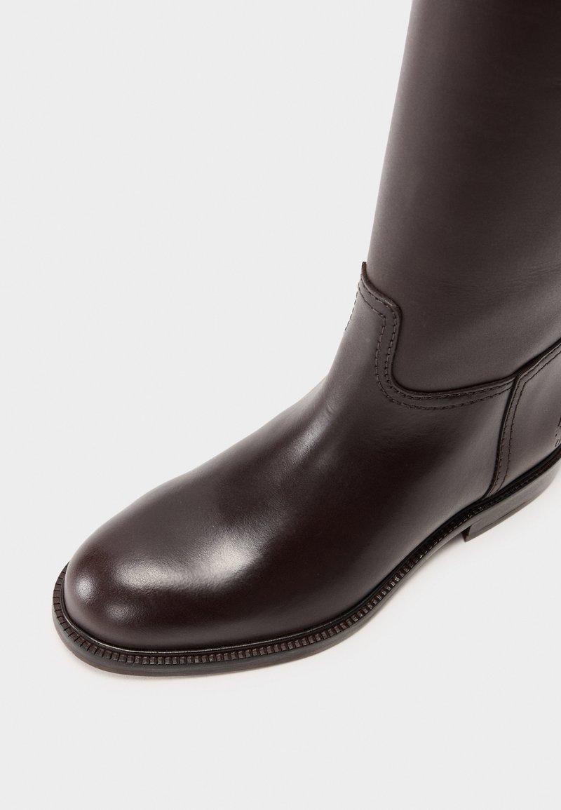 Brązowy skórzany kozak do kolan o gładkiej teksturze, okrągłym nosku, detalach przeszycia i niskim obcasie. Odpowiedni na różne okazje.