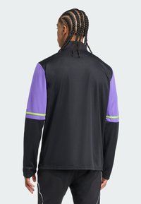 Schwarze Langarm-Sportjacke mit lila Ärmeln und grünen sowie weißen Akzentstreifen. Glatter, leichter Stoff und figurbetontes Design.