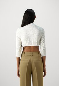 Biely krajkový crop top s trojštvrťovými rukávmi, so zúženým lemom. Spárovaný s béžovými nohavicami s vysokým pásom a zadnými vreckami.