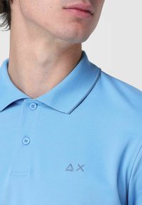 Polo shirt azzurro chiaro realizzato in tessuto testurizzato, presenta un colletto e tre bottoni, con un discreto design del logo sul petto.