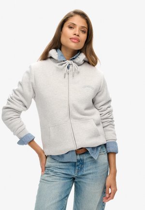 Sweat à capuche zippé gris clair avec cordon de serrage, poches avant et logo brodé. Porté sur une chemise en denim et assorti avec un jean bleu.