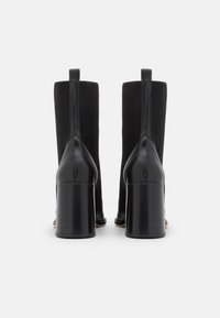 Botines negros con tacón de cuero y parte superior de punto, con caña recta, punta cerrada y un acabado texturizado.