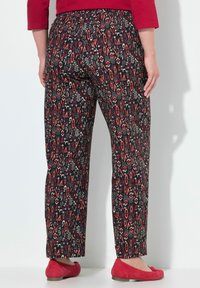 Černé kalhoty se vzorem, které mají červené a bílé geometrické designy, vyrobené z lehkého materiálu, v kombinaci s červenými balerínami.