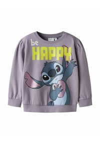 Lilla genser med ribbestrikkede mansjetter og hals, med en tegneseriefigur som holder et hjerte og teksten "be HAPPY" i fete, lyse farger.