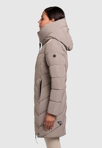 Polstret lang frakke i lys beige med høj krave, chevron-quilting, sorte lynlåse, et hængemærke og hætte. Elegant design med en glat tekstur.