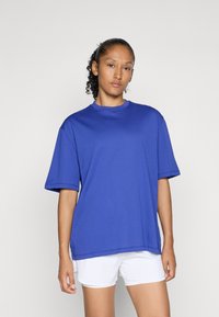 Kék pamut póló rövid ujjú, kerek nyakú, laza szabású. Egyszerű dizájn, nincsenek minták vagy díszítések, fehér sorttal viselve.