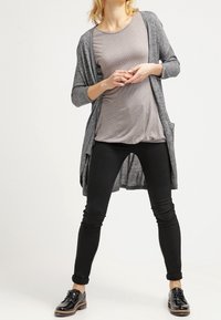 Šedý dlouhý kardigan přes světlý šedý top s puntíky, doplněný černými slim-fit džíny a černými šněrovacími botami. Hladký materiál, volný střih.