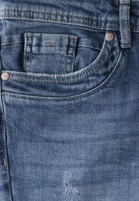Jeans de mezclilla azul oscuro con un pequeño bolsillo frontal, remaches de cobre y un parche desgastado en la tela. Textura suave y diseño resistente.