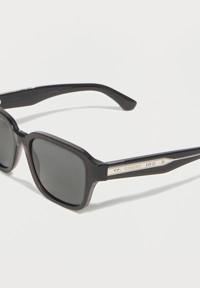 Μαύρα γυαλιά ηλίου με τετράγωνο πλαίσιο, γκρι φακούς και το λογότυπο της Burberry στα πλαινά, τοποθετημένα σε λευκό φόντο.