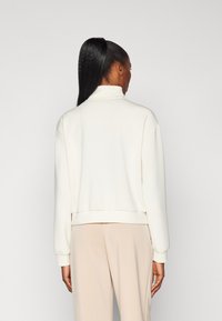 Witte sweatshirt met hoge hals, ontspannen pasvorm, ribgebreide manchetten en tailleband; soepele textuur en minimalistisch ontwerp.