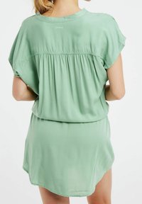 Robe verte à manches courtes en tissu doux. Présente un détail froncé au dos et un ourlet arrondi. Comprend le logo "Protest" au niveau du col.