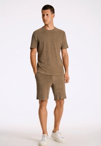 T-shirt marrone, con texture, e pantaloni corti abbinati. L'outfit presenta un collo rotondo e una vestibilità comoda, abbinato a sneakers bianche.
