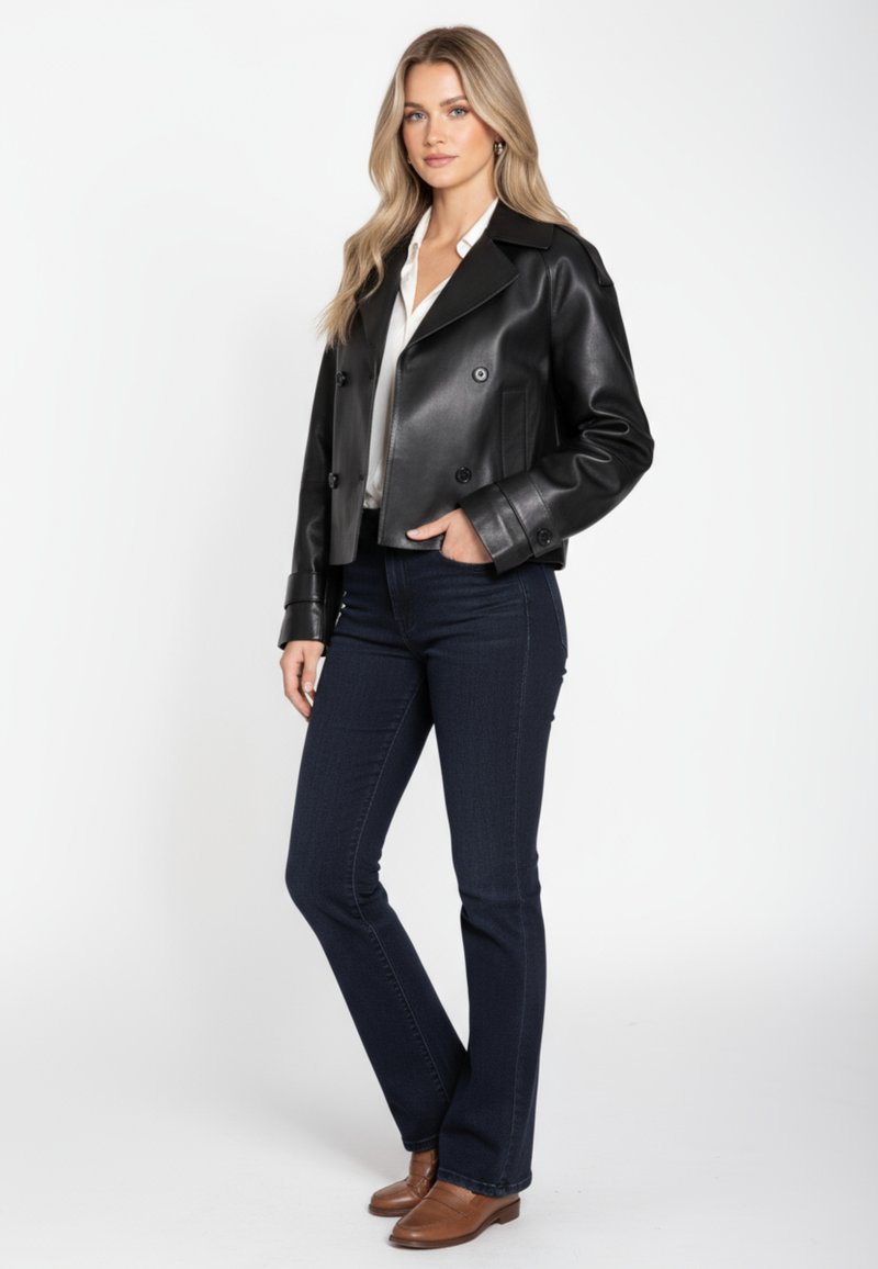 Zwart leren cropped double-breasted jack, gecombineerd met donkerblauwe flare jeans en bruine loafers, afgebeeld tegen een witte achtergrond.