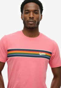 Roze katoenen t-shirt met korte mouwen, voorzien van een horizontaal gestreept detail in rood, groen, blauw en marineblauw, en een klein logo op de borst.
