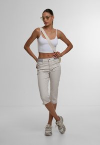 Weißes kurzes Oberteil, hellbeige Caprihosen und graue Sneaker. Hat einen geraden Schnitt und subtile Nähte, kombiniert mit einer Umhängetasche.