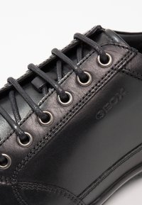 Pantofii din piele neagră cu șireturi împletite, gauri metalice pentru șireturi și cusături vizibile. Prezintă un logo subtil și o textură netedă în partea superioară.