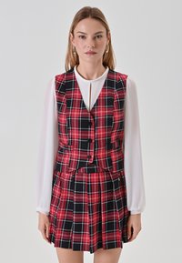 Completo in tessuto scozzese rosso e nero composto da gilet e gonna, abbinato a una camicia bianca a maniche lunghe. Include bottoni, pieghe e un colletto.